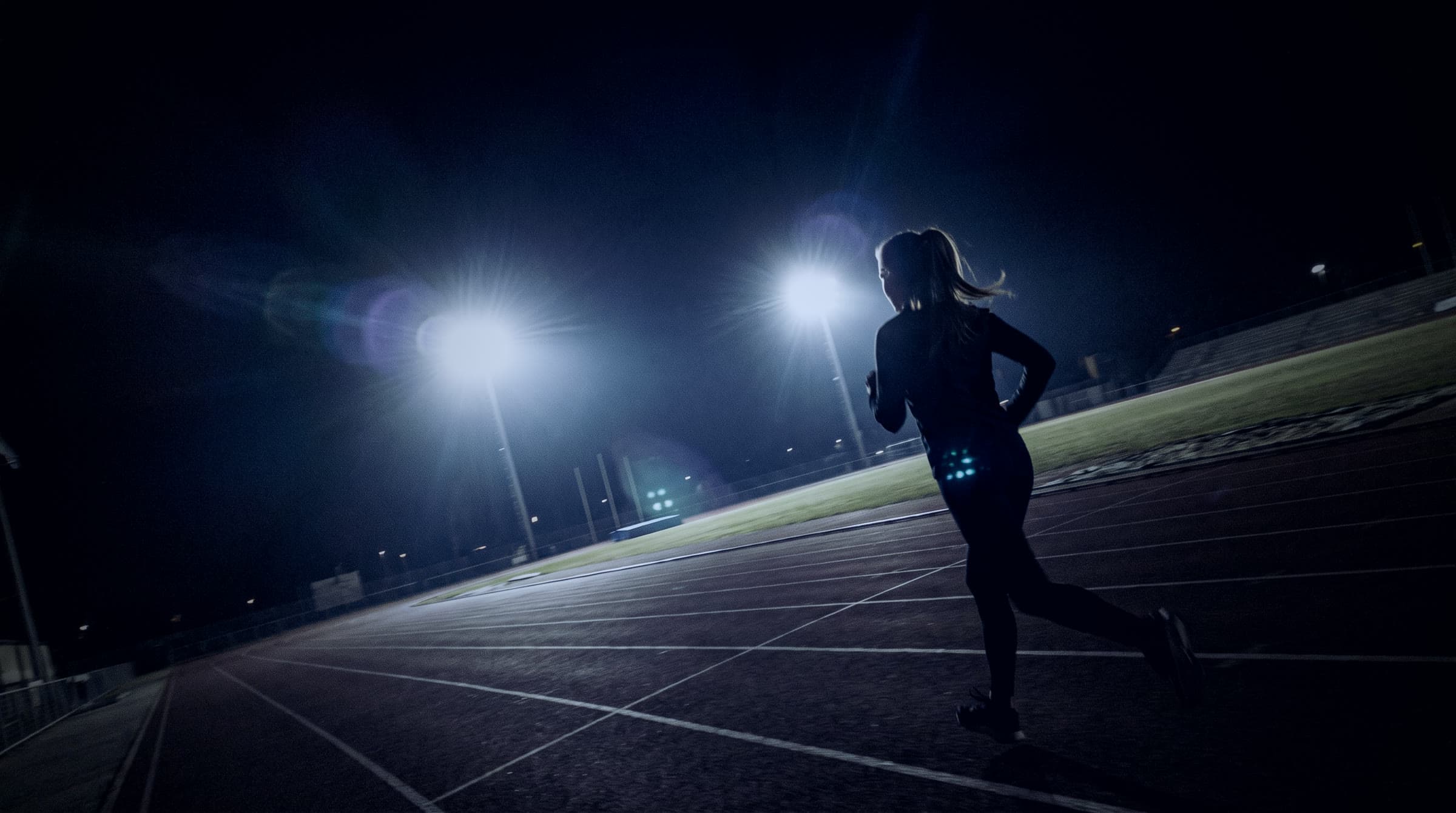 Opositora corriendo series de noche en una pista de atletismo iluminada por los focos